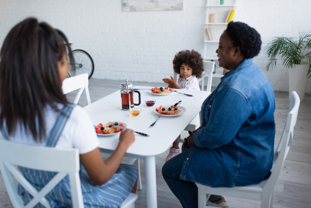 Afrikanisch-amerikanisches Kind zeigt mit der Hand in der Nähe von Mama und Oma beim Frühstück in der Küche - Foto, Bild