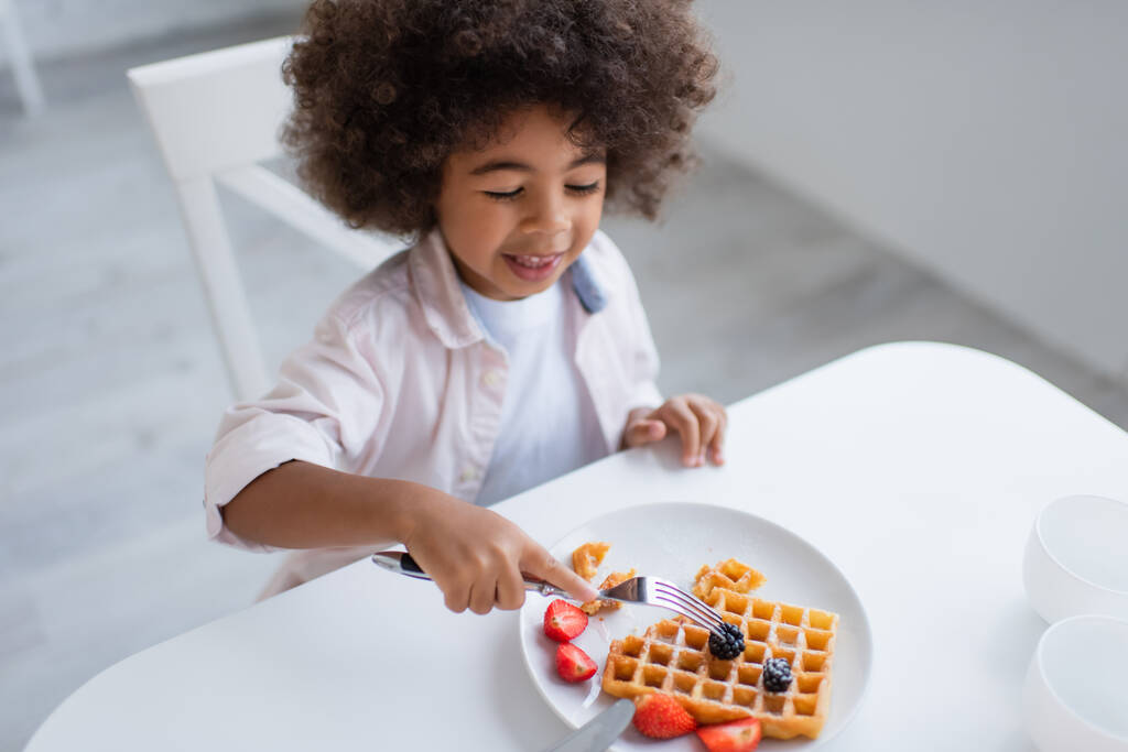 high angle view of african american girl with fork near tasty waffle with fresh berries - Photo, Image