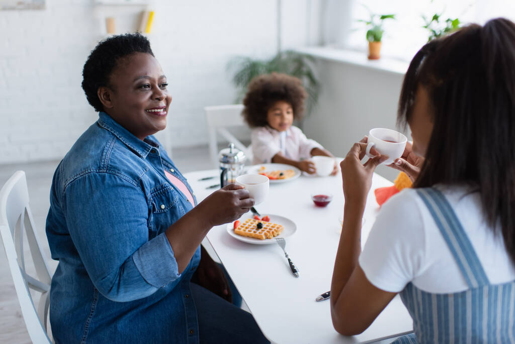 szczęśliwy Afroamerykanka kobieta je śniadanie z córką i wnuczką w kuchni - Zdjęcie, obraz