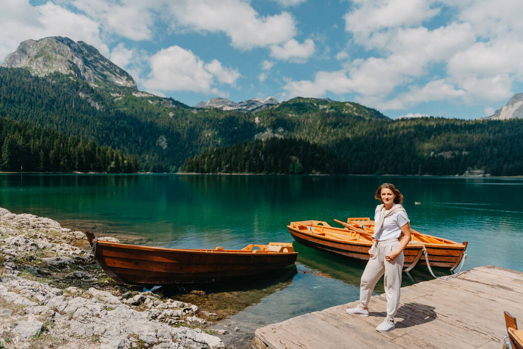 Dívka se dívá na Černé jezero s rybářskými čluny, lesy a horami v národním parku Durmitor v Černé Hoře. Turista má kouzelný výhled na jezero, jehličnatý les a kouzelný - Fotografie, Obrázek