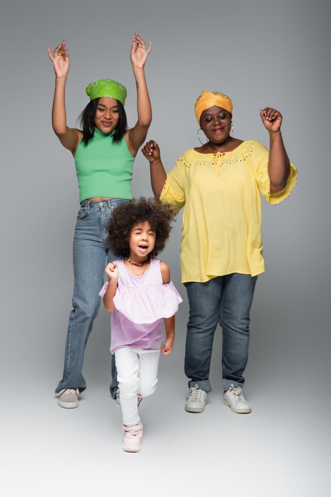 cheerful african american women with girl in trendy clothes dancing on grey - Photo, Image