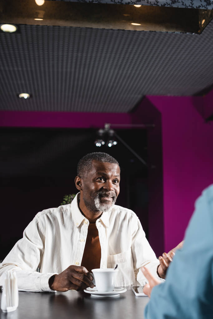 щасливий старший афроамериканський чоловік жестикулює під час розмови з розмитим другом в барі
 - Фото, зображення