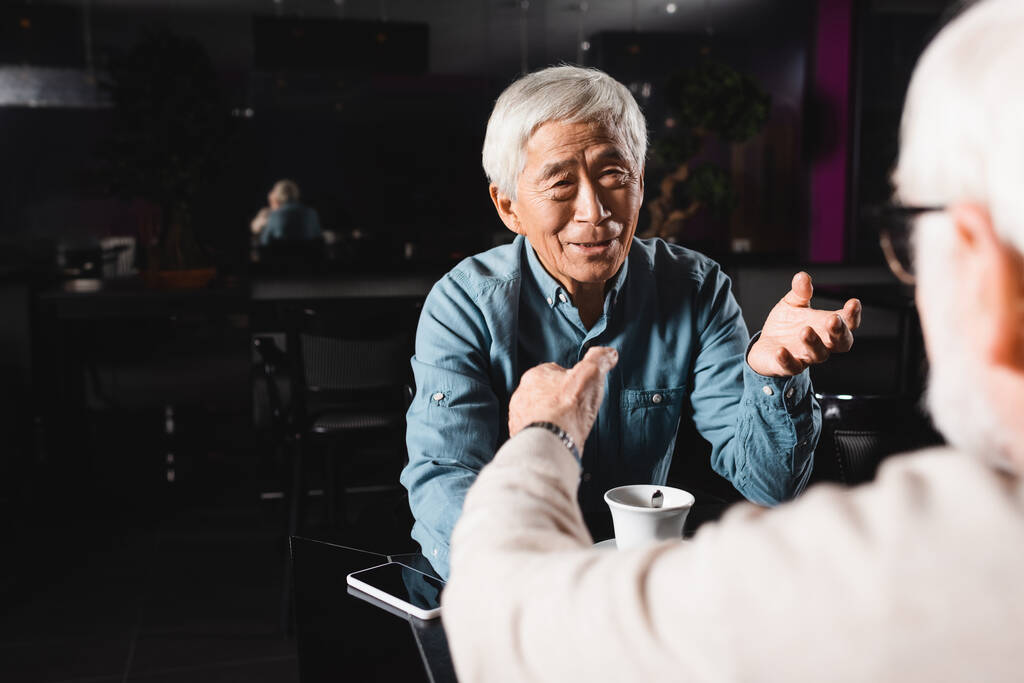 sênior asiático homem e seu amigo borrado gestos durante a conversa no café - Foto, Imagem