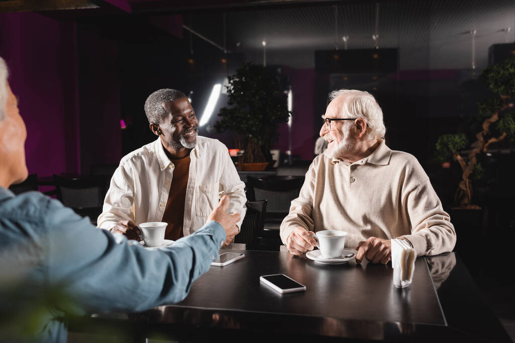 amis multiethniques aînés souriant lors d'une conversation dans un café - Photo, image