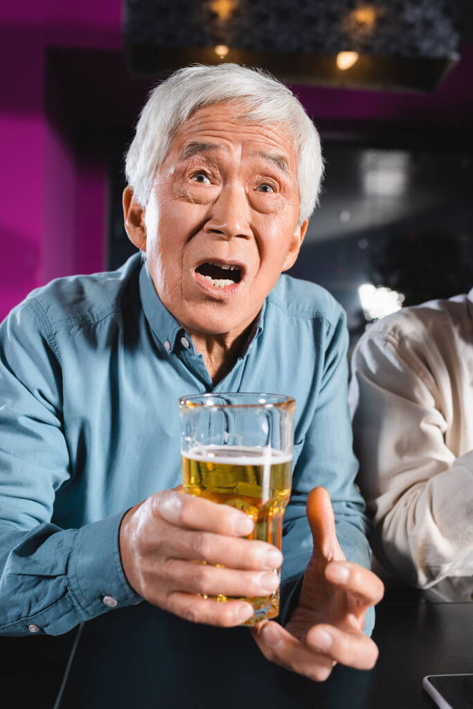 σοκαρισμένος Ασιάτης με ένα ποτήρι μπύρα βλέποντας πρωτάθλημα σε αθλητικό μπαρ - Φωτογραφία, εικόνα