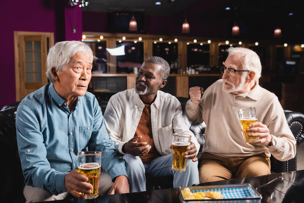 Senioren interrassische Freunde gestikulieren, während sie mit asiatischen Freund in der Kneipe sprechen - Foto, Bild