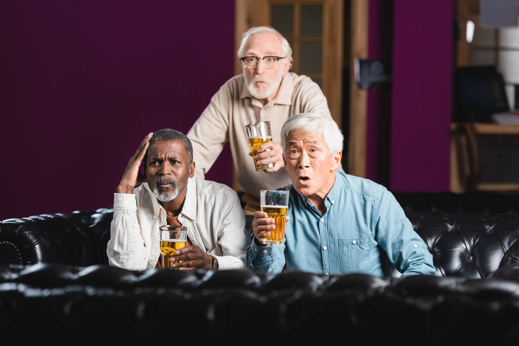 σοκαρισμένος ηλικιωμένους πολυεθνικούς φίλους με ποτήρια μπύρας βλέποντας ποδόσφαιρο πρωτάθλημα στην παμπ - Φωτογραφία, εικόνα