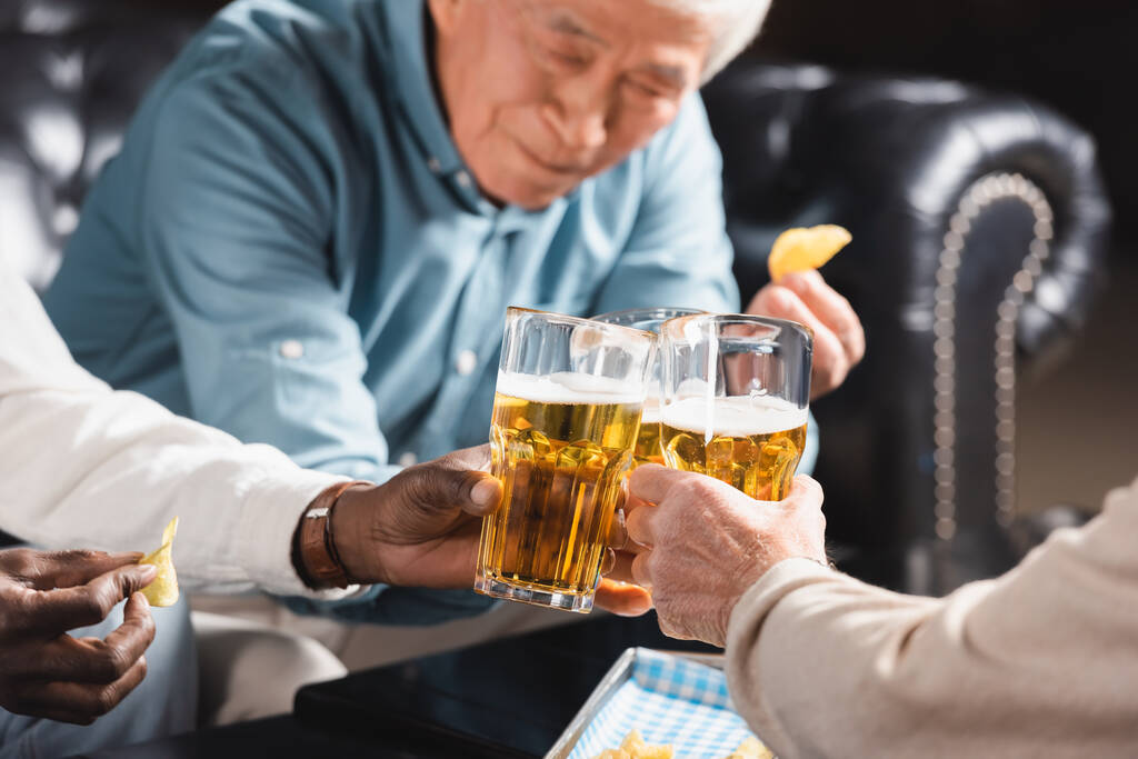 desenfocado asiático hombre tintineo cerveza vasos con multicultural amigos en pub - Foto, imagen