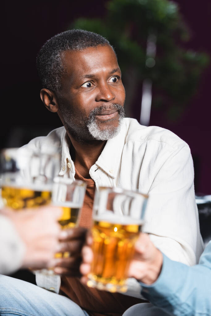 asombrado sénior africano americano hombre tintineo borrosa cerveza vasos con amigos en pub - Foto, imagen
