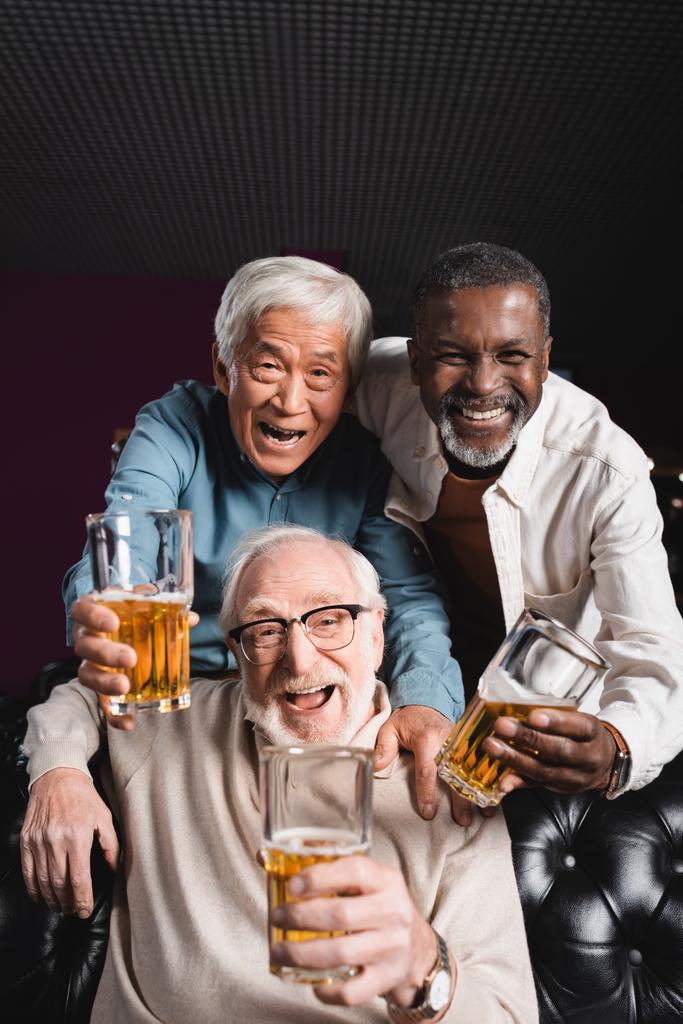 aufgeregte, ältere multikulturelle Freunde mit Biergläsern, die in der Bar in die Kamera schauen - Foto, Bild