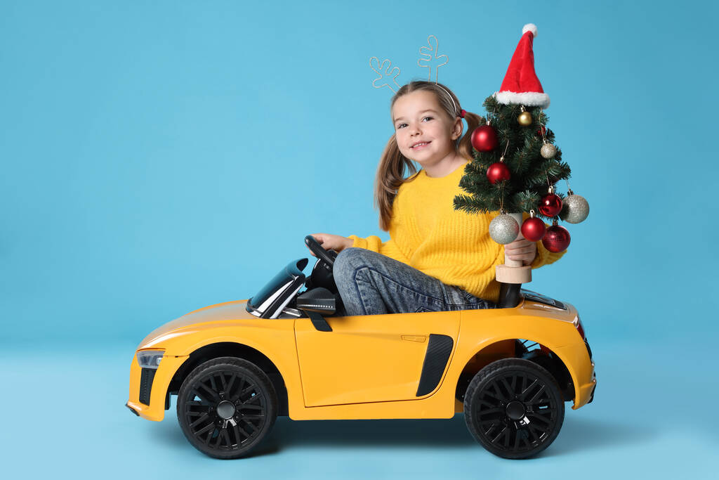かわいいです女の子とともにクリスマスツリー運転子供の電気おもちゃ車上のライトブルーの背景 - 写真・画像