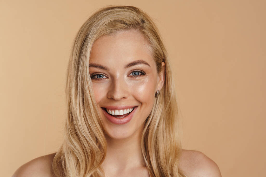 Bellezza immagine di una giovane donna bionda felice sorridente con i capelli lunghi spalle nude in piedi su sfondo beige - Foto, immagini