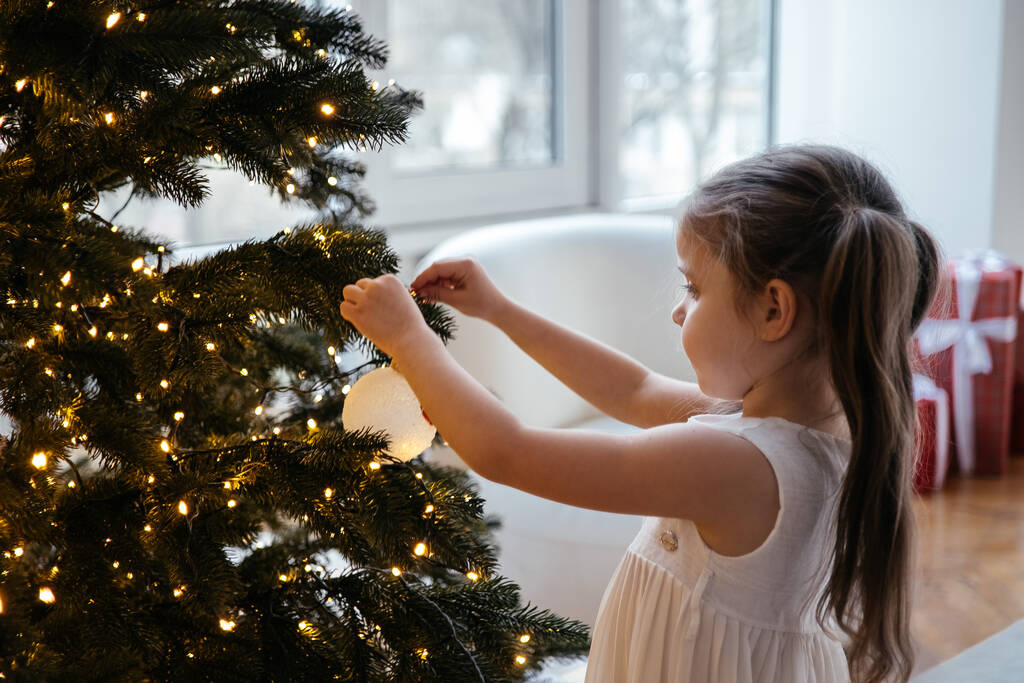 peuter meisje versieren kerstboom thuis  - Foto, afbeelding