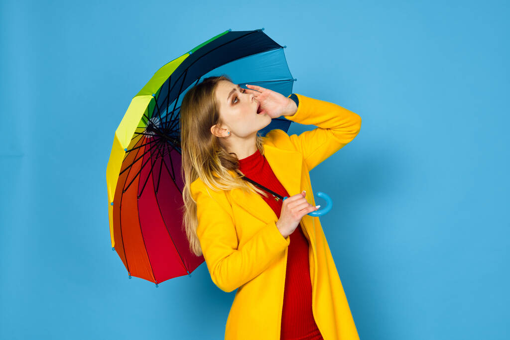mujer en abrigo amarillo paraguas multicolor posando fondo azul - Foto, Imagen