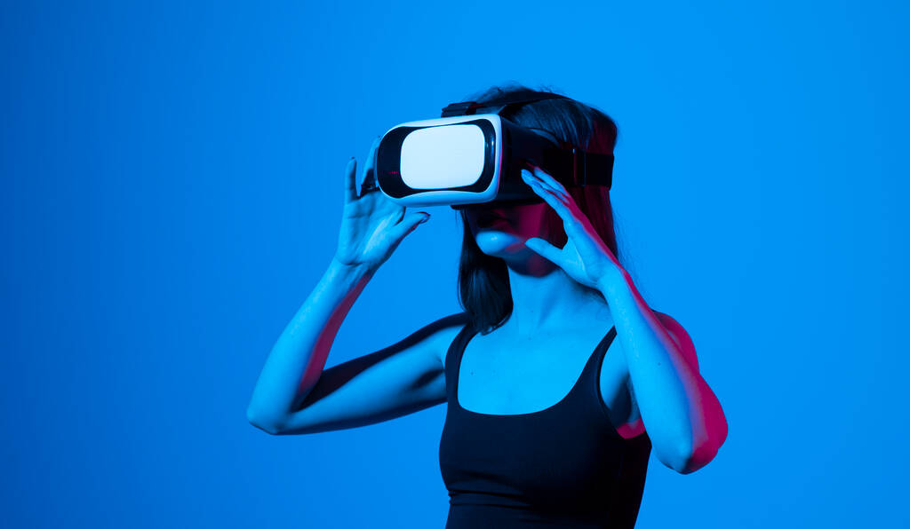 Portrét mladé ženy hrající v brýlích VR v neonovém světle na modrém pozadí. Koncept moderní přístroje a technologie. Budoucí koncept technologie. Virtuální realita hraní. - Fotografie, Obrázek