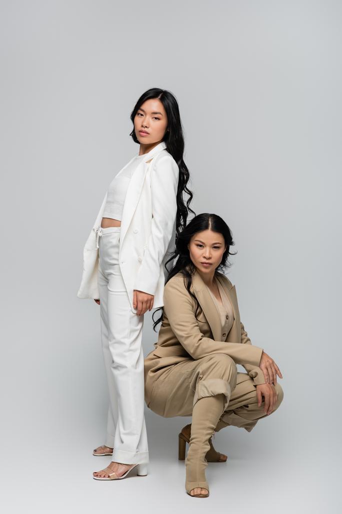 comprimento total da moda asiática mãe em terno bege e elegante jovem adulto filha posando em cinza - Foto, Imagem