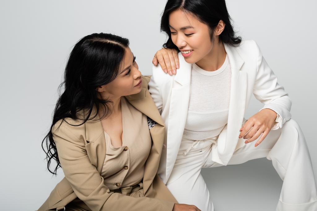стильная азиатская мать и счастливая молодая взрослая дочь смотрят друг на друга на сером - Фото, изображение