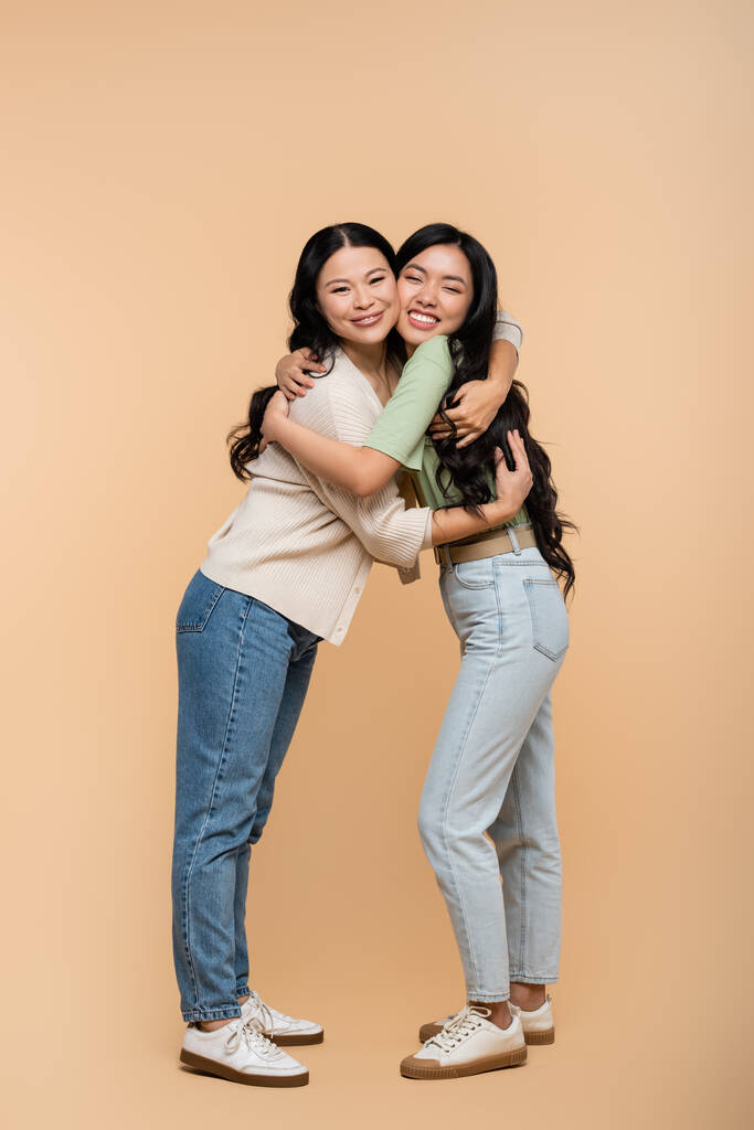 full length of cheerful asian mother and daughter hugging on beige  - Photo, Image