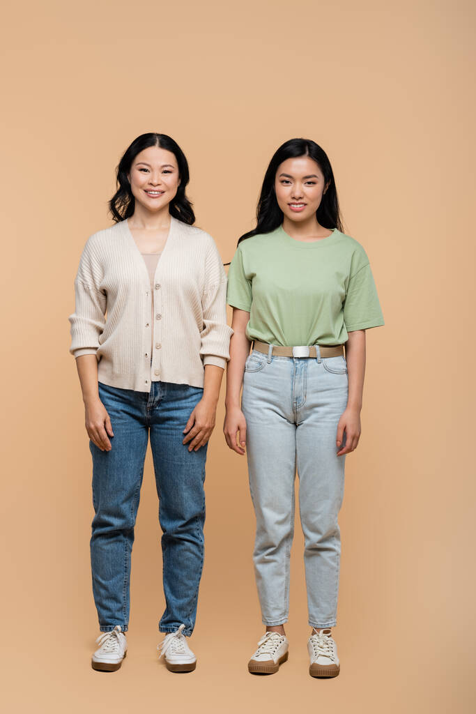 full length of cheerful asian mother and adult daughter standing on beige  - Photo, Image