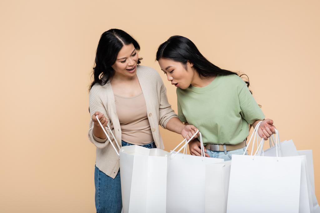 yllättynyt aasialainen nainen etsii ostoskassi lähellä äiti eristetty beige - Valokuva, kuva