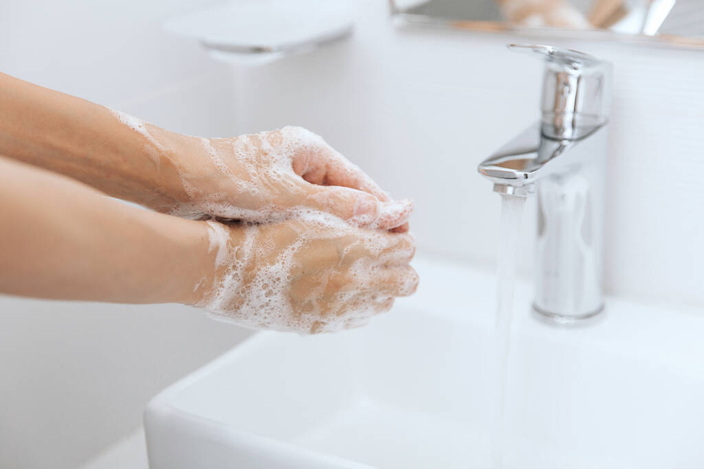 Lavarse las manos bajo el grifo de agua corriente. Lavarse las manos frotándose con jabón para la prevención del virus de la corona, higiene para dejar de propagar el virus de la corona en el baño público o. Concepto de higiene detalle de la mano - Foto, Imagen