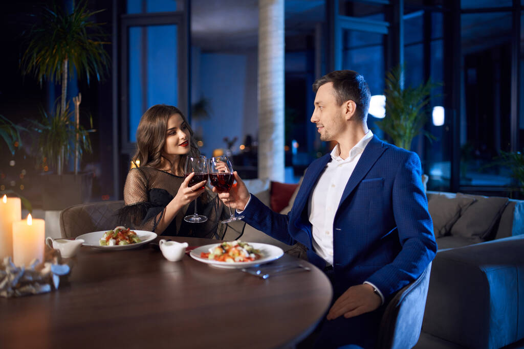 Schönes Paar sitzt bei Wein und Salat am Tisch - Foto, Bild