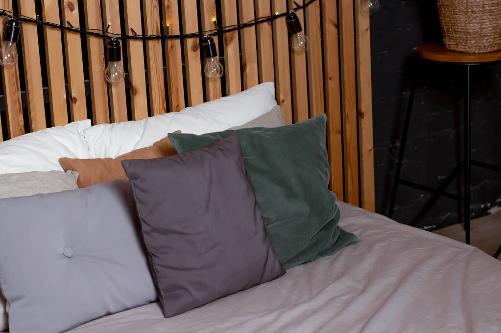 Μαξιλάρια στο κρεβάτι σε γκρι, πράσινο, λευκό και καφέ με φόντο έναν ξύλινο τοίχο. - Φωτογραφία, εικόνα