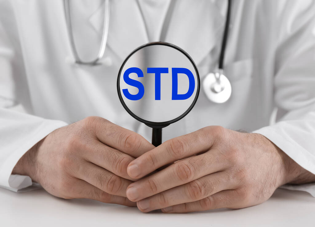 Лікар тримає збільшувальне скло з абревіатурою STD на білому столі, крупним планом
 - Фото, зображення