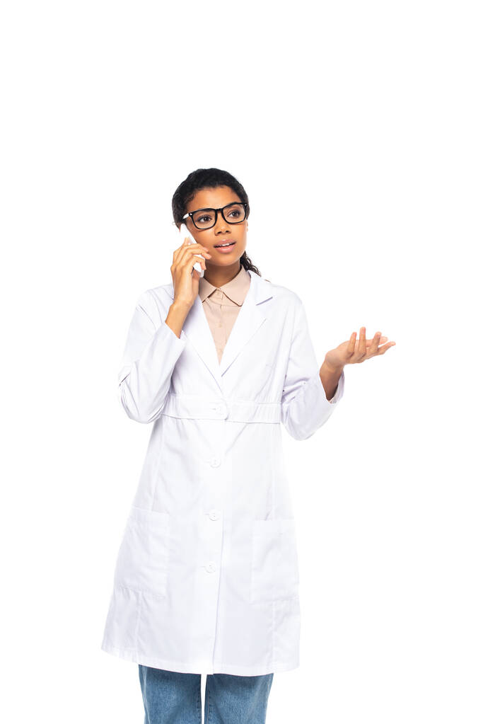 Лікар - афроамериканець у окулярах говорить на смартфоні, ізольованому на білому  - Фото, зображення