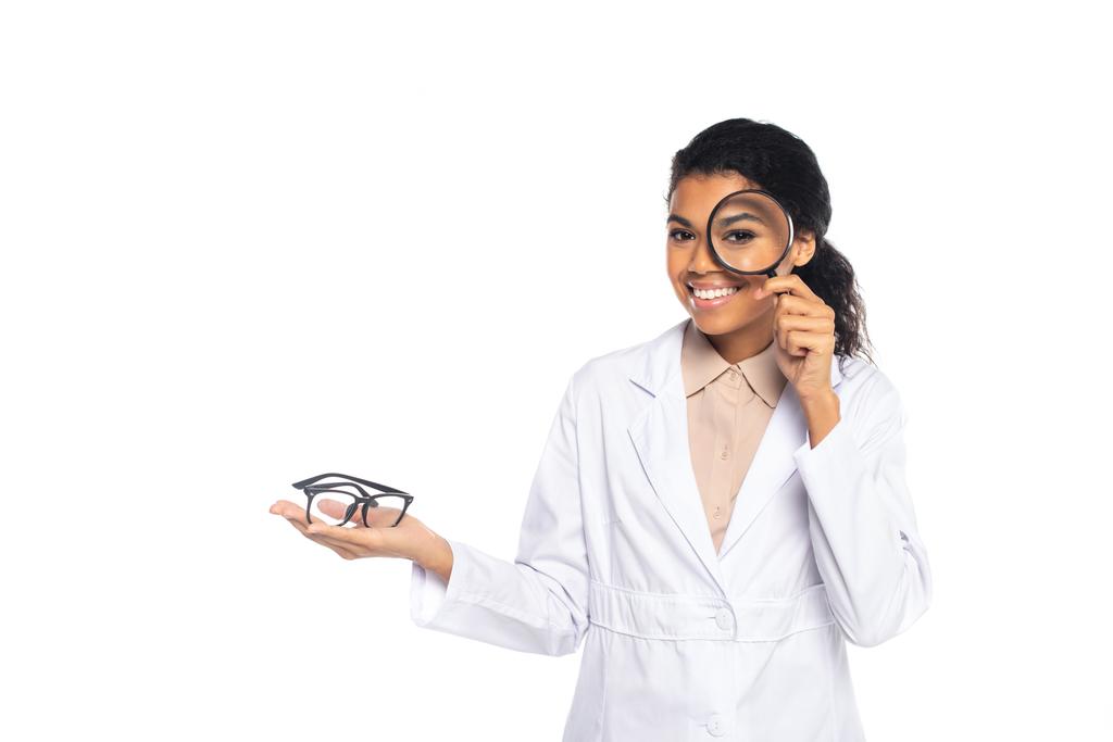 Усміхнений афроамериканський окуліст тримає окуляри і збільшує скло ізольовано на білому
  - Фото, зображення