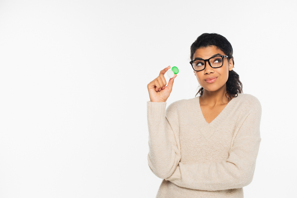 Pensive african american woman in eyeglasses holding contact lenses isolated on white - Photo, Image