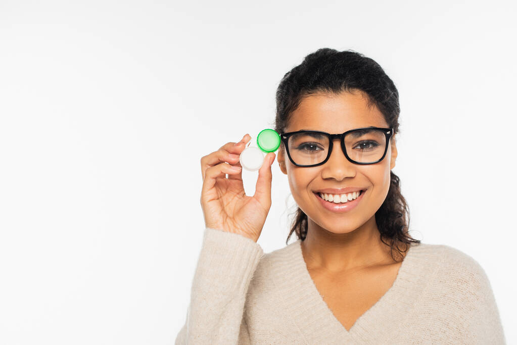 Smiling african american woman in eyeglasses holding contact lenses and looking at camera isolated on white - Photo, Image