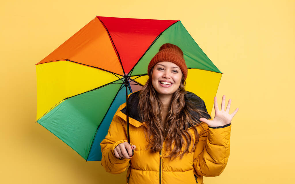 ヒスパニック系の女性は笑顔で友好的に見える5番目を示しています。傘の概念 - 写真・画像