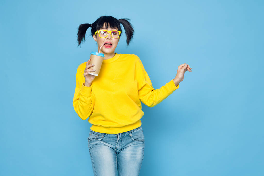 mujer alegre con coletas en suéter amarillo beber fondo azul - Foto, Imagen