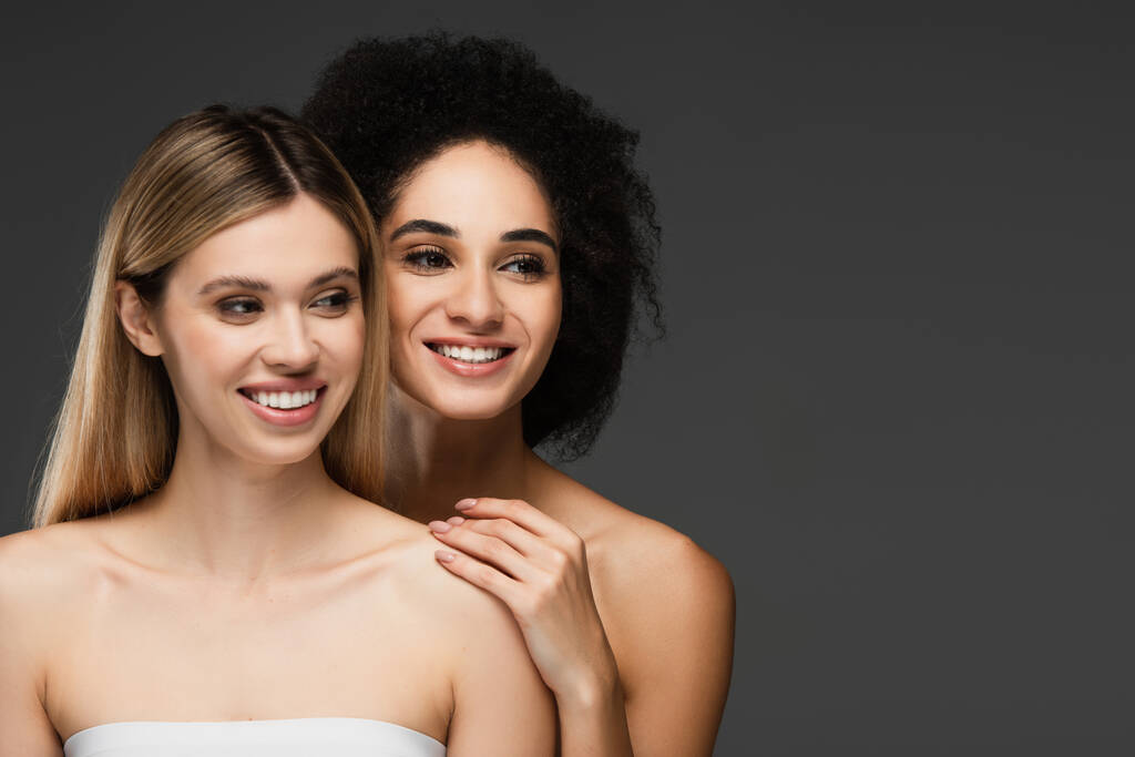 mujeres multiétnicas felices con hombros desnudos y la piel perfecta mirando hacia otro lado aislado en gris - Foto, imagen