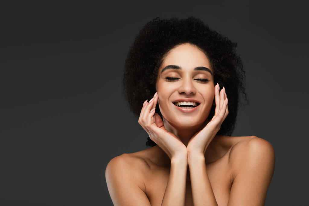 幸せアフリカ系アメリカ人女性目を閉じて顔に完璧な肌に触れるグレーに孤立 - 写真・画像