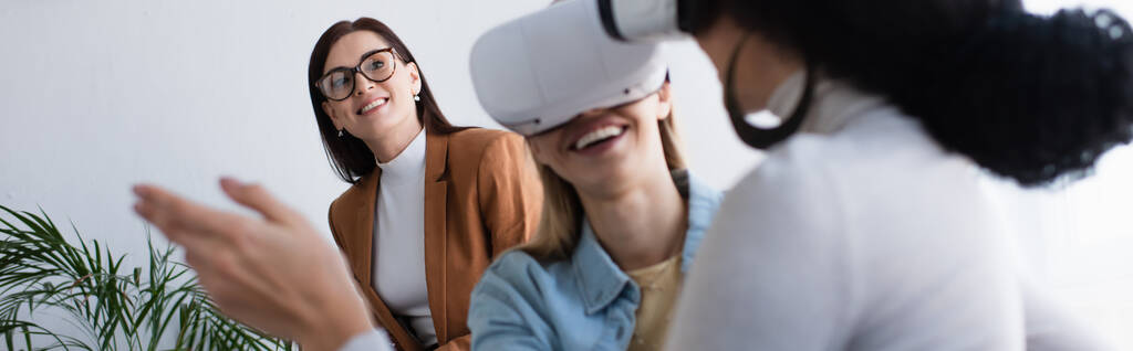 psychologist in eyeglasses smiling near interracial lesbian couple gaming in vr headsets, banner - Photo, Image