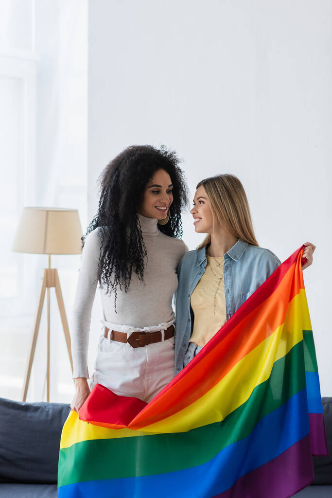 jeunes lesbiennes multiethniques femmes souriant à l'autre tout en tenant lgbt drapeau - Photo, image