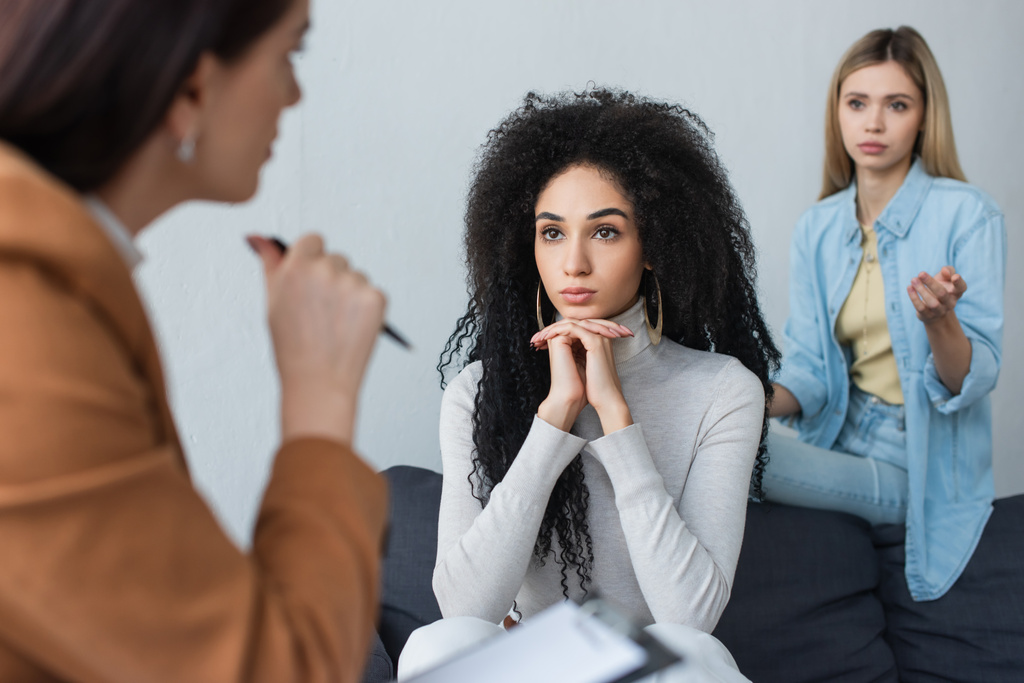zdenerwowana para międzyrasowych lesbijek słuchających niewyraźnego psychologa podczas konsultacji - Zdjęcie, obraz