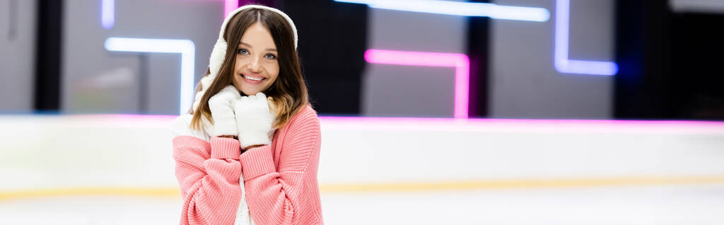 joyful young woman in ear muffs and scarf on ice rink, banner - Photo, Image