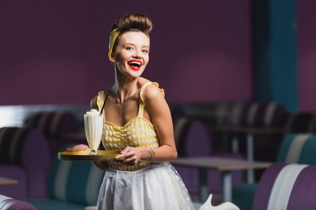 положительный пин-ап официантка держит поднос с молочным коктейлем в кафе  - Фото, изображение
