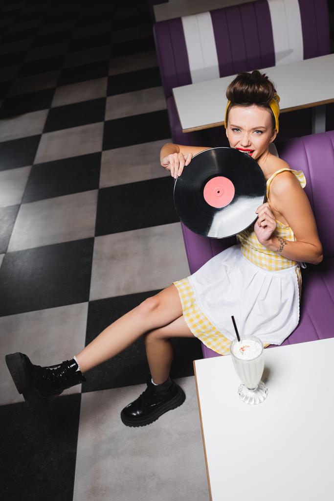 high angle view of young pin up woman biting retro vinyl disc  - Photo, Image