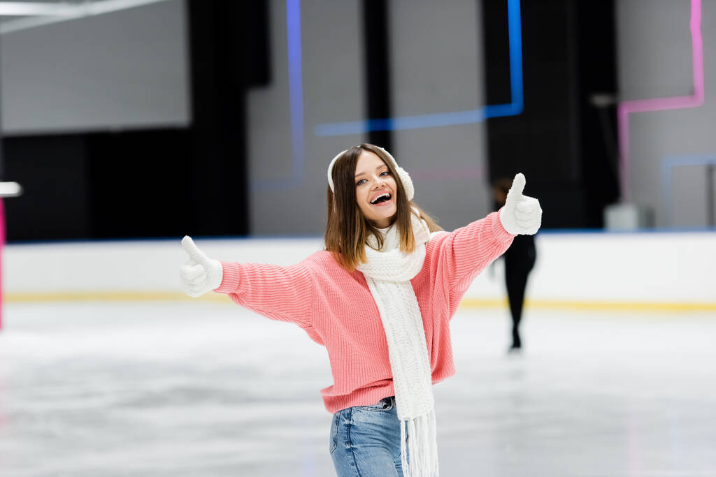 verbaasd jonge vrouw in roze trui tonen duimen tot op de ijsbaan  - Foto, afbeelding