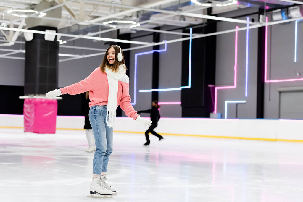 pleine longueur de jeune femme gaie en tenue d'hiver patiner avec les mains tendues sur la patinoire  - Photo, image