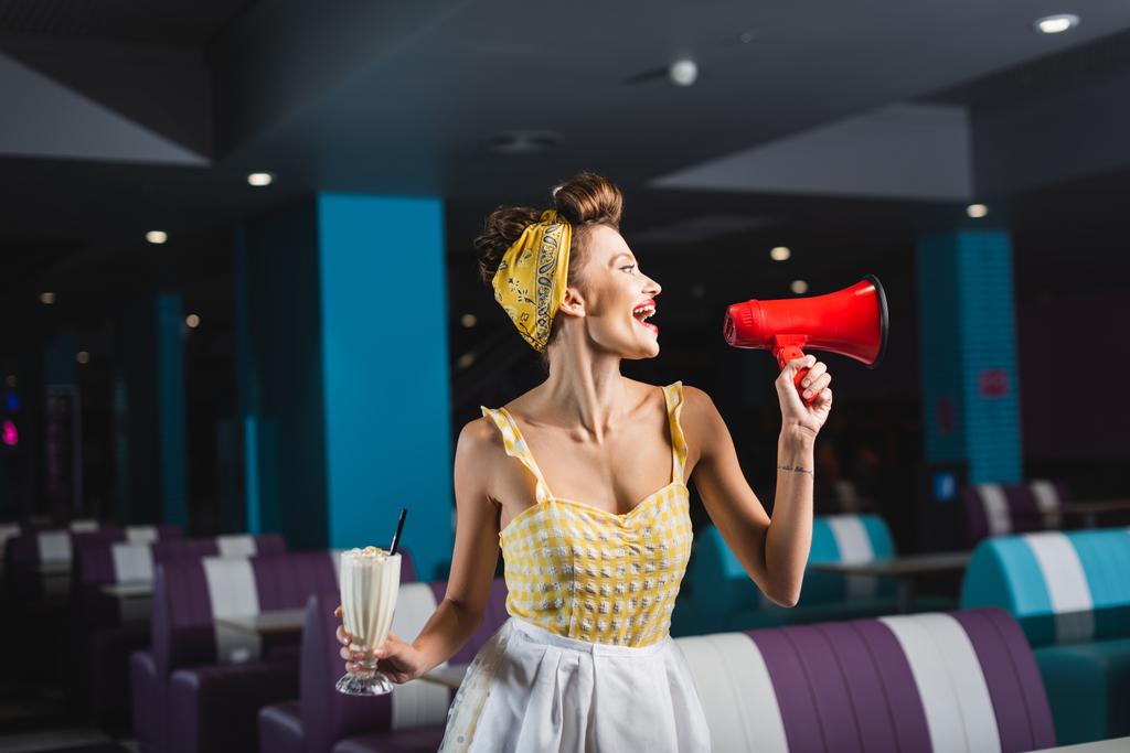 Ευτυχισμένος καρφίτσα σερβιτόρα κρατώντας milkshake και ουρλιάζοντας σε μεγάφωνο  - Φωτογραφία, εικόνα