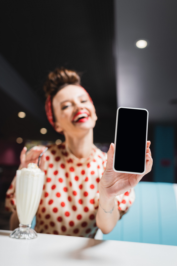 verschwommene und glückliche Pin-up-Frau hält Smartphone mit leerem Bildschirm  - Foto, Bild