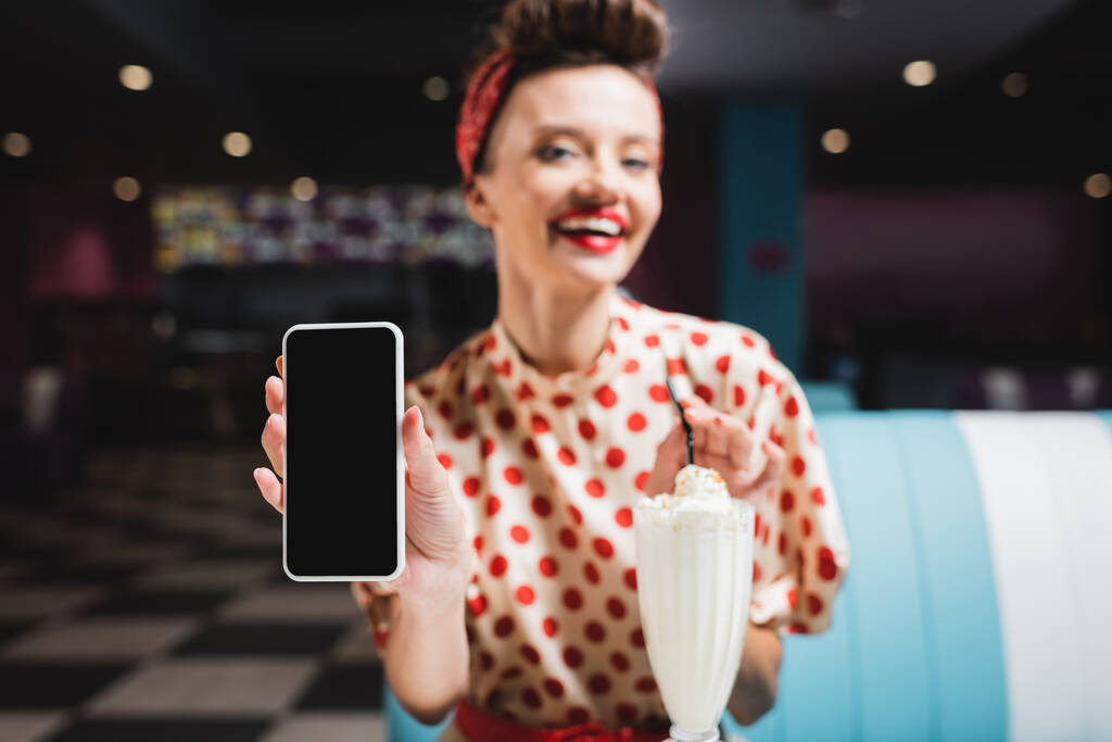 alfiler mujer borrosa y sonriente sosteniendo teléfono inteligente con pantalla en blanco  - Foto, imagen