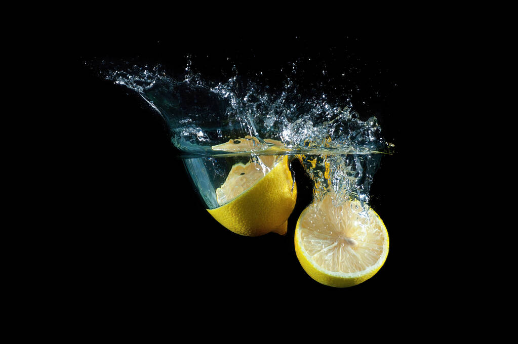 Dvě poloviny čerstvých citronů ponořených hluboko do vody s cákancemi na černém pozadí - Fotografie, Obrázek