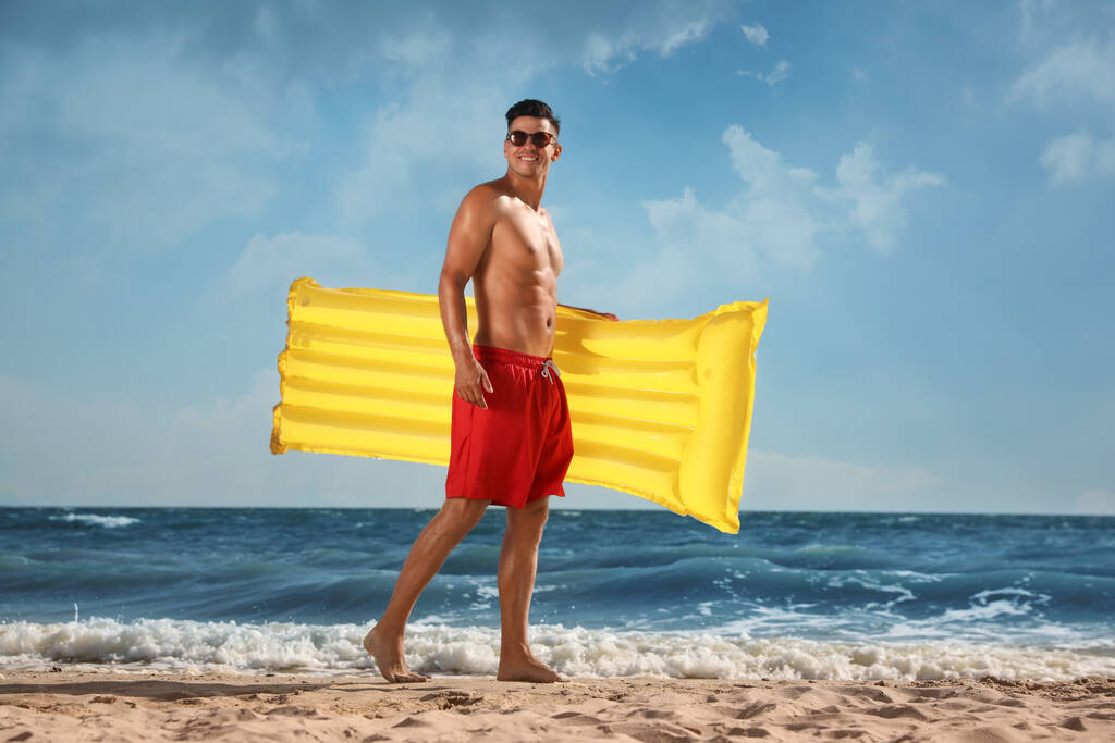 Uomo con materasso gonfiabile giallo in spiaggia - Foto, immagini