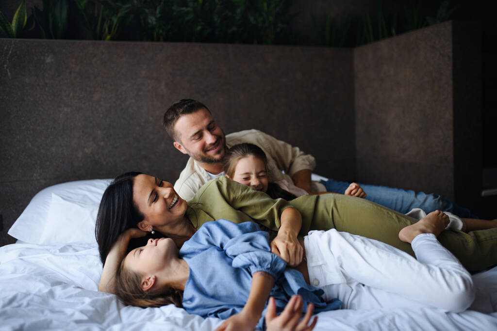 Boldog fiatal család két gyerekkel feküdt az ágyon a szállodában, nyári szünet. - Fotó, kép